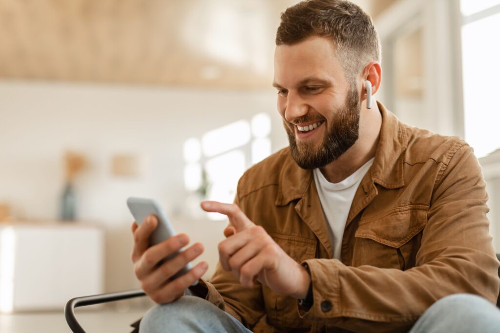 happy man using mobile phone wearing earbuds texting home
